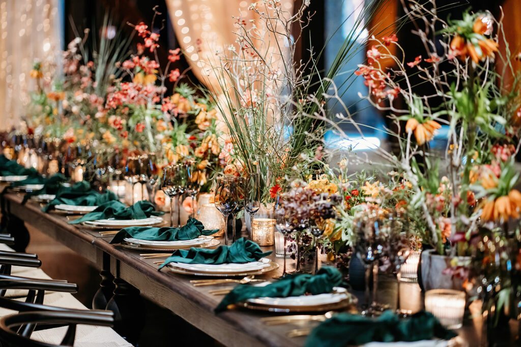 Long wooden wedding table styled with organic florals, textured linens, and candlelight for a timeless wedding design