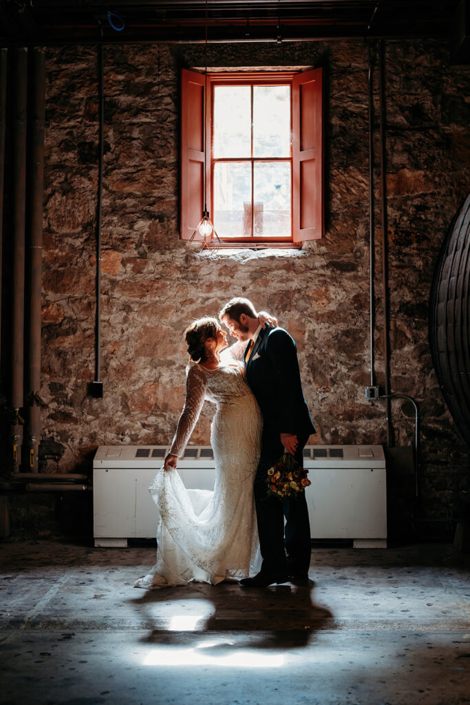 Wedding couple sharing an intimate moment inside a stone room with natural window light and soft shadows