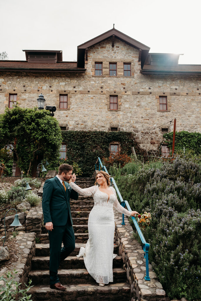 Bride and groom walking down stone steps at a vineyard wedding venue surrounded by greenery and soft light