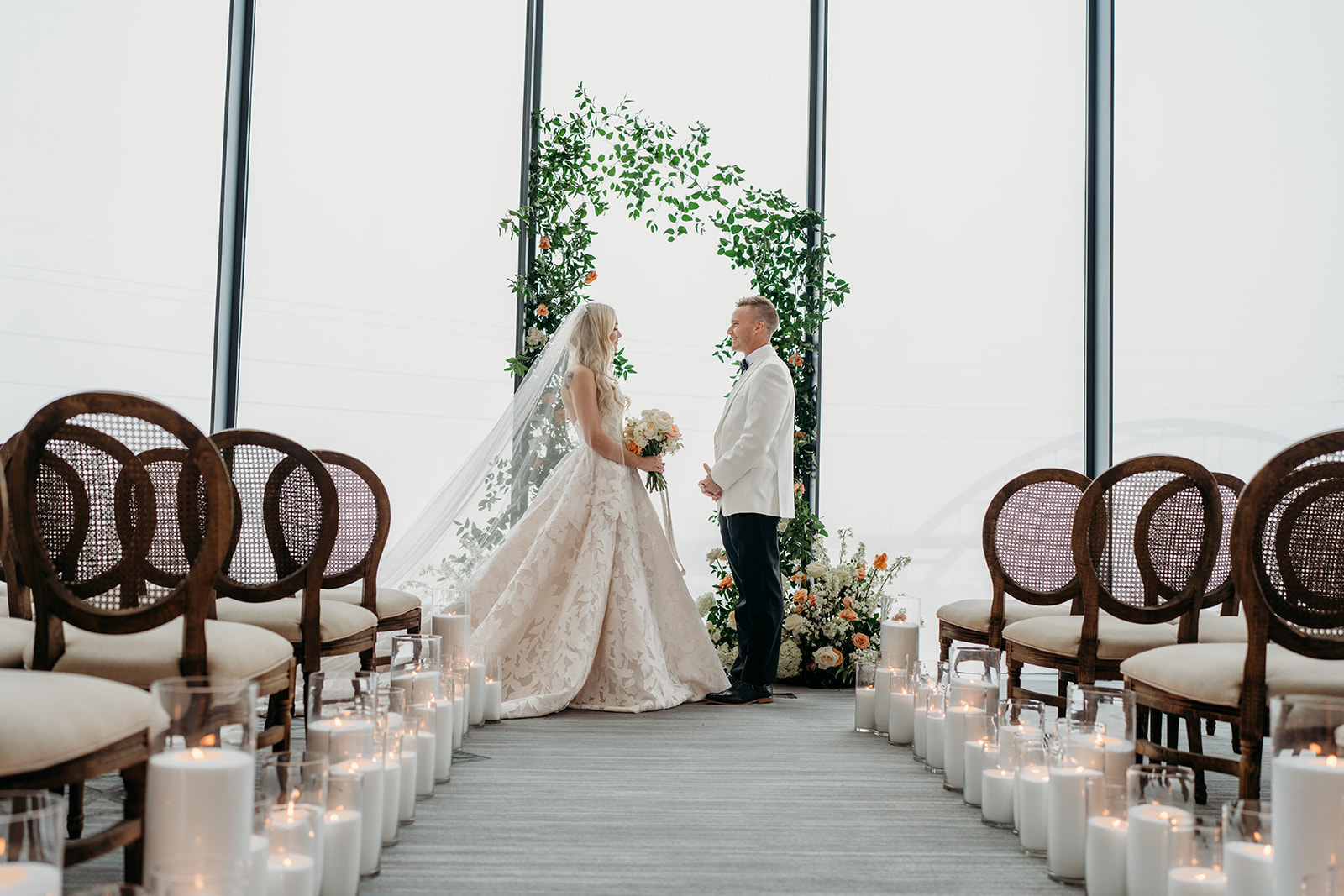 Wedding ceremony setup with candle-lined aisle, greenery arch, and soft neutral design in natural light